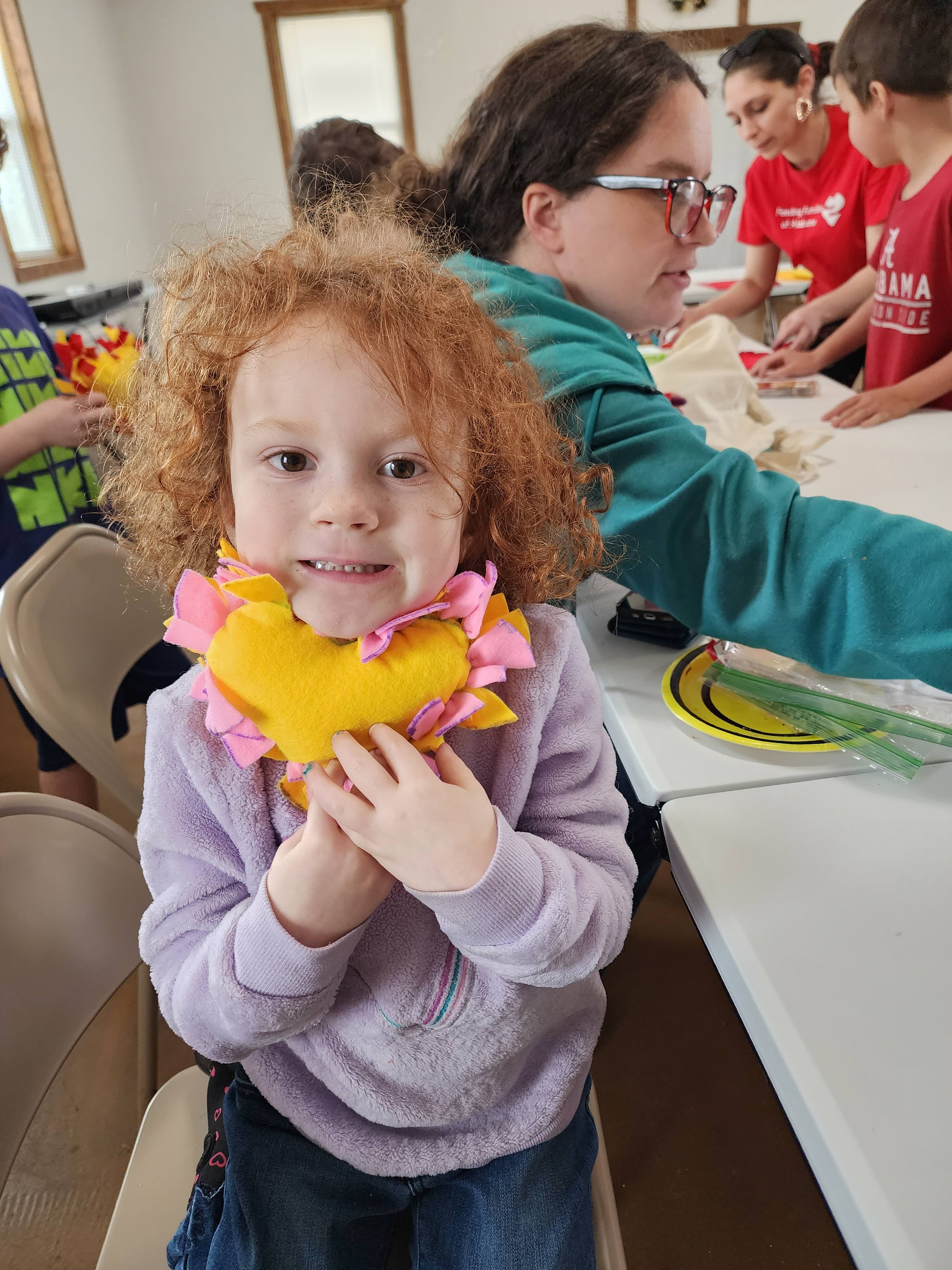 A young girl smiles for the camera and holds her yellow heart pillow